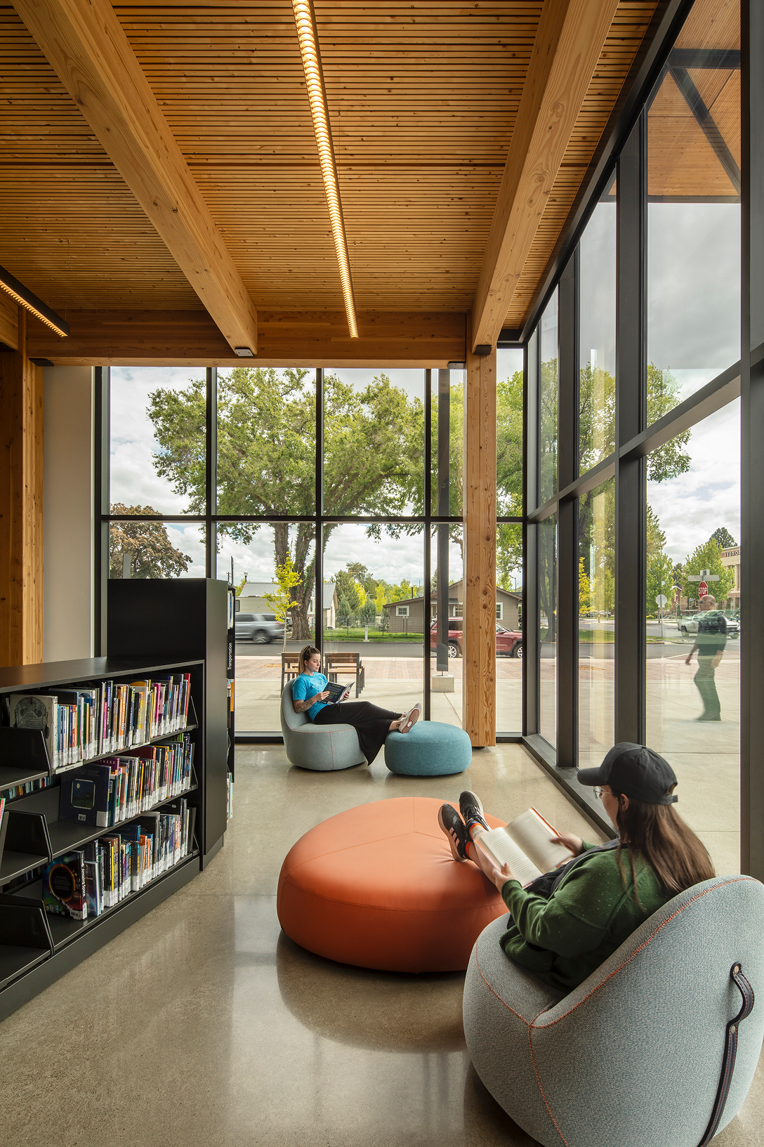 Exposed timber columns, beams, and wood ceiling beside floor-to-ceiling windows at Redmond Library in Redmond, Oregon.