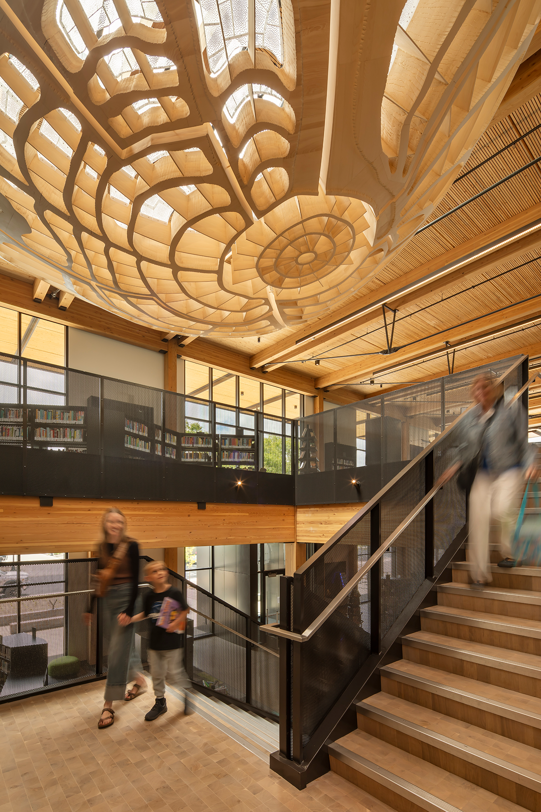 Redmond Library staircase beneath a sculptural skylight, surrounded by exposed timber beams and wood ceilings in Redmond, Oregon. Redmond Library in Redmond, Oregon.